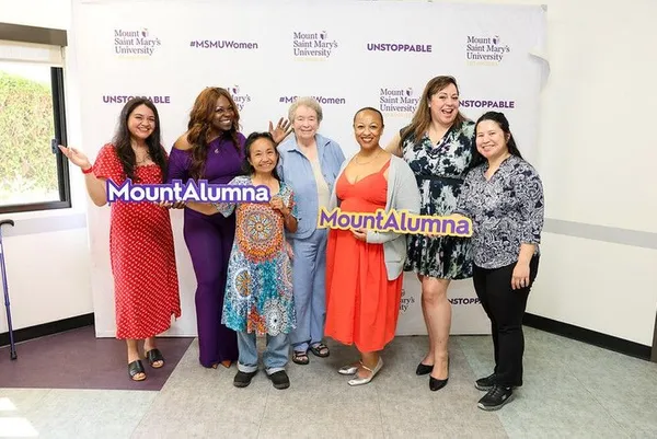 group of alumna smiling in front of a msmu backdrop with msmu branded photo props