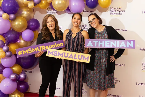 three alums smiling in front of a MSMU back-drop