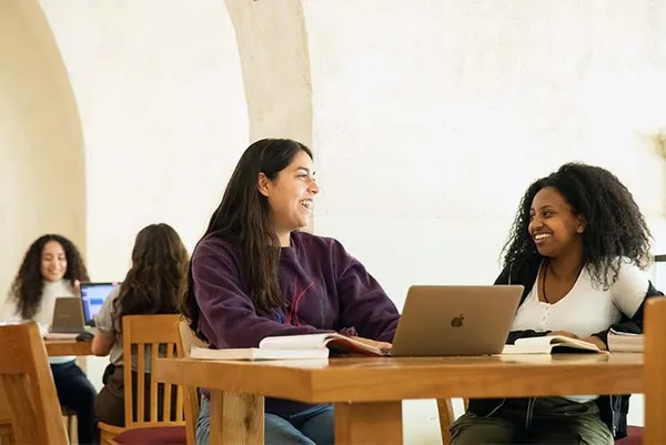 students sitting at a table with laptops studying and smiling