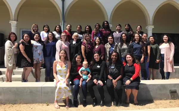 A large group photo outside in front of an arched walkway