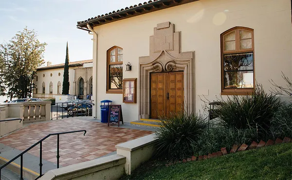 The front double doors of a short building with two windows on either side of the door.
