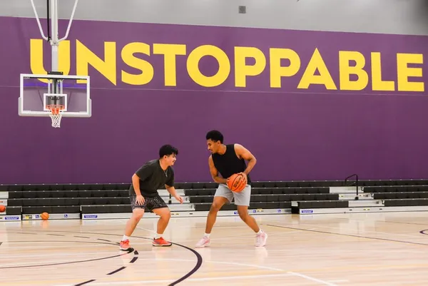 two male students in workout clothes playing indoor basketball in the gym, with the word unstoppable painting on the wall behind them