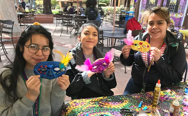 Three students holding up brightly colored masks.