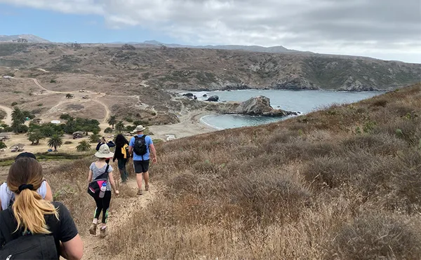 Students hiking along a path with a small cove in the distance.