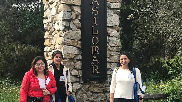 Three people standing in front of a sign that says 