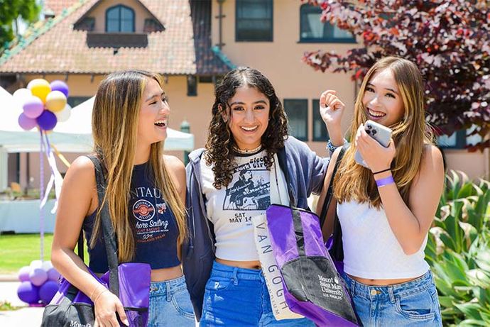 three students smiling holding 91ɬ�� Saint Mary's gear