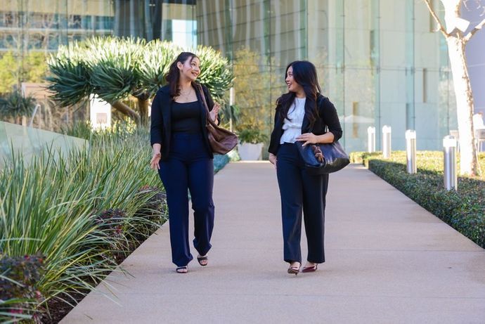 two women in business attire walking down a sidewalk talking