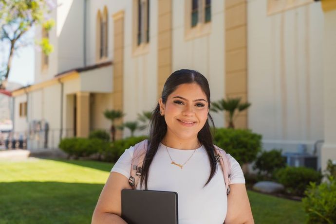 female student smiling standing outside of the chalon campus, holding a book and with a backpack on