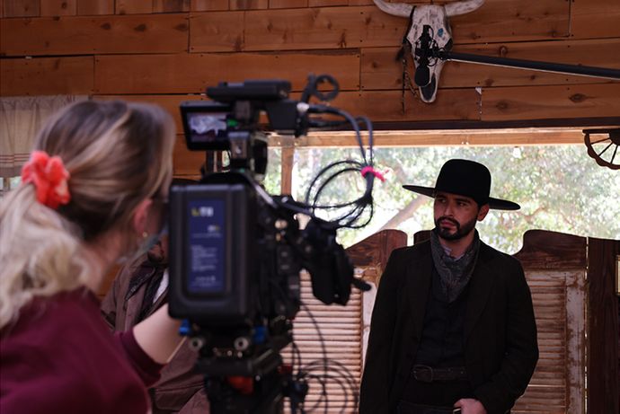 Woman filming man wearing hat on a western film set