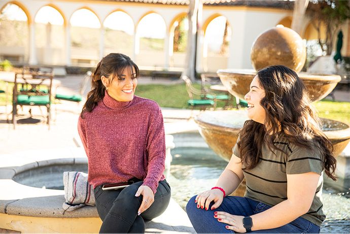 two female students sitting on a fountain ledge on the chalon campus laughing while talking