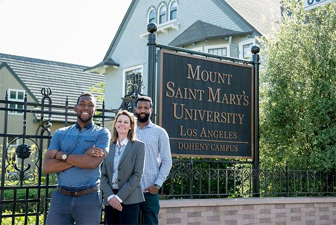 Three graduate students smiling standing in front of a 91ɬ�� campus sign