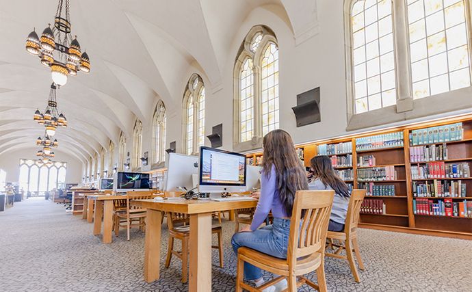 A large library hall with a student using a desktop computer in the foreground