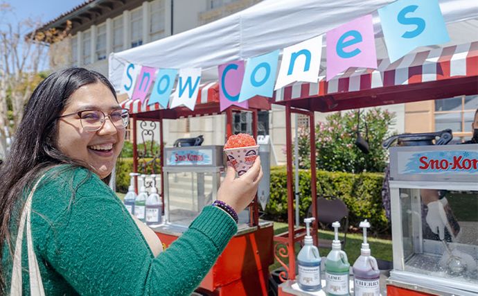 A student holding a snowcone in front of a snowcone booth