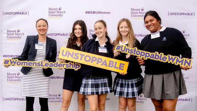 group of students posing with signs in front of back-drop