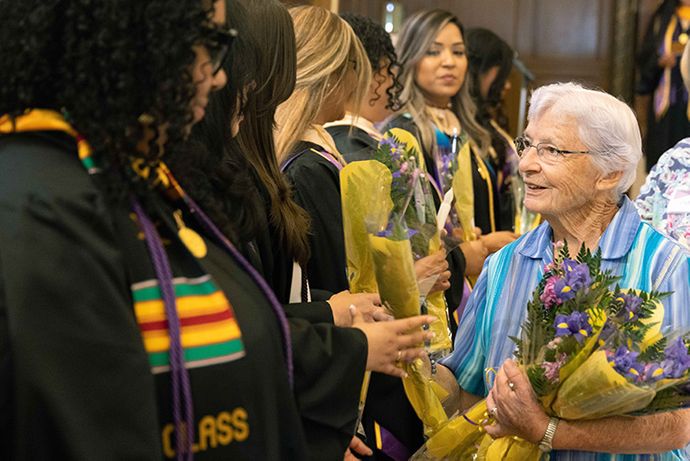 An older woman handing flowers to 91ɬ�� Graduates
