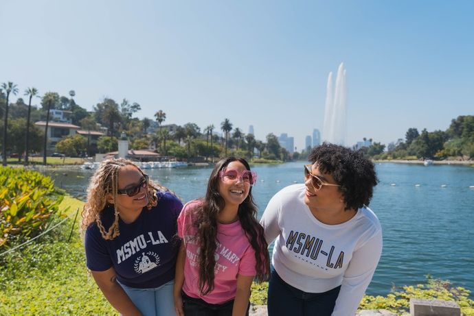 three female students in 91ɬ�� gear smiling in front of the pond at echo park