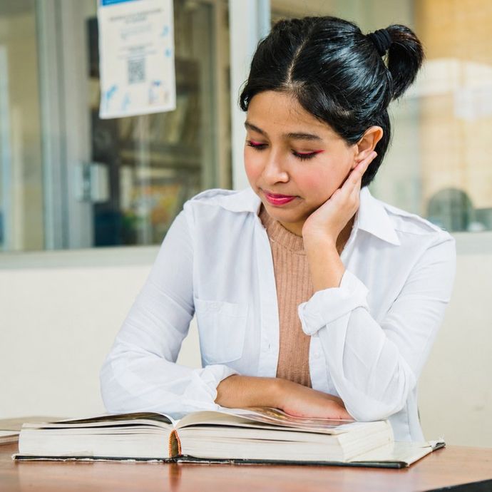 female student in white coat sitting reading a book