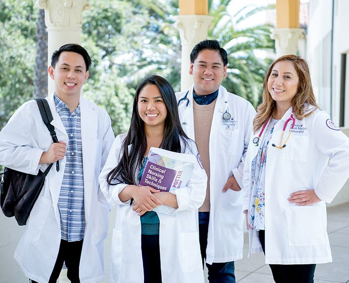 four nursing students in white coats smiling with books and backpacks at Chalon campus