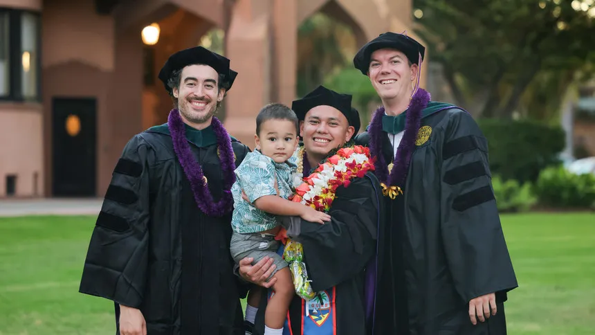 Three DPT graduates smiling in front of the doheny mansion. One graduate is holding a baby.
