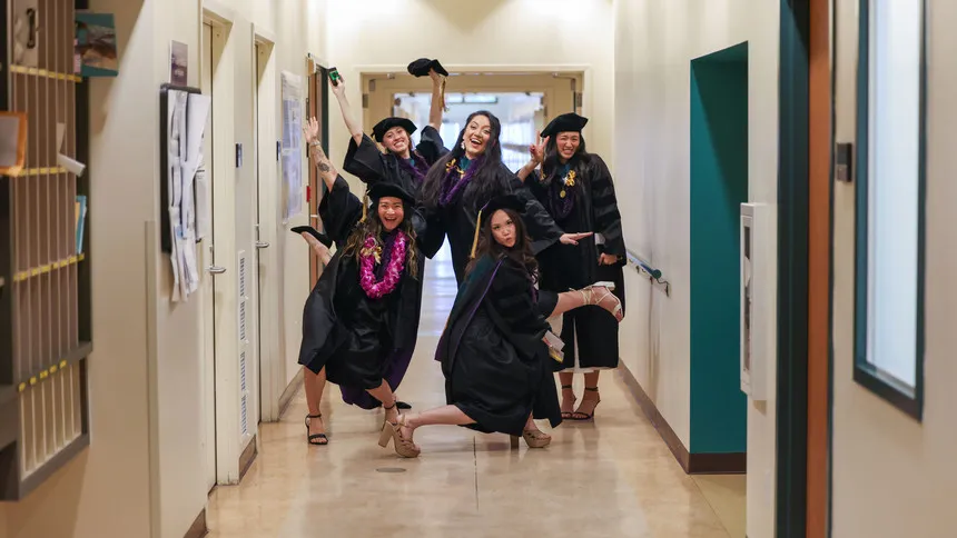 Graduate students in robes posing and smiling in a school hallway