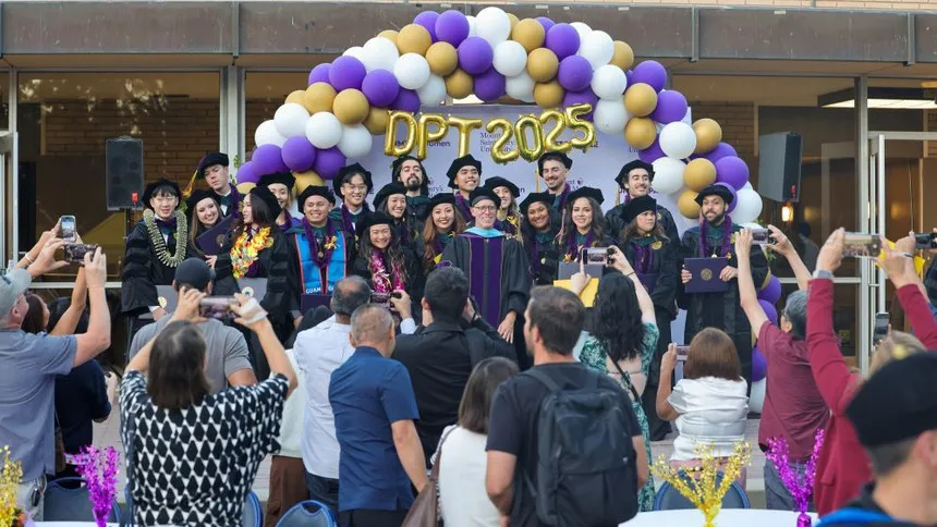 DPT graduates smiling in front of a crowd of their friends and family