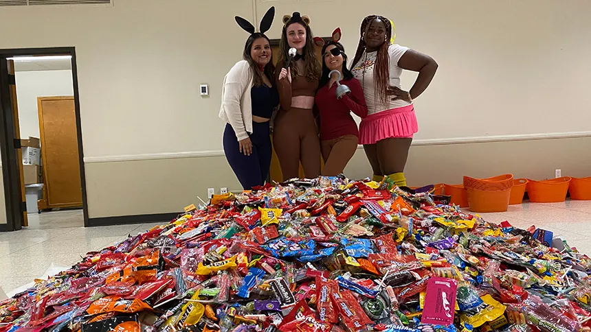 Women posing in costumes behind a large pile of halloween candy